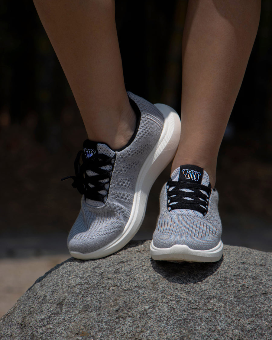 Close-up of feet wearing gray Woolloomooloo lace-up sneakers with black laces and white soles, standing on a rock
